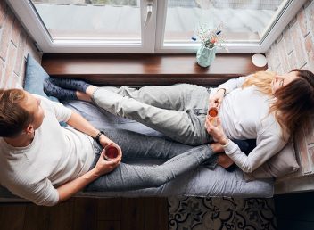 Top view of couple in love who spending time together, looking out the window, drinking warm tea and dreaming about future. Cozy sitting area by window which creating calm romantic atmosphere.
